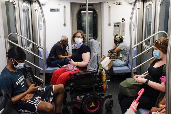 A woman in a wheelchair wearing a mask rides the New York City subway.